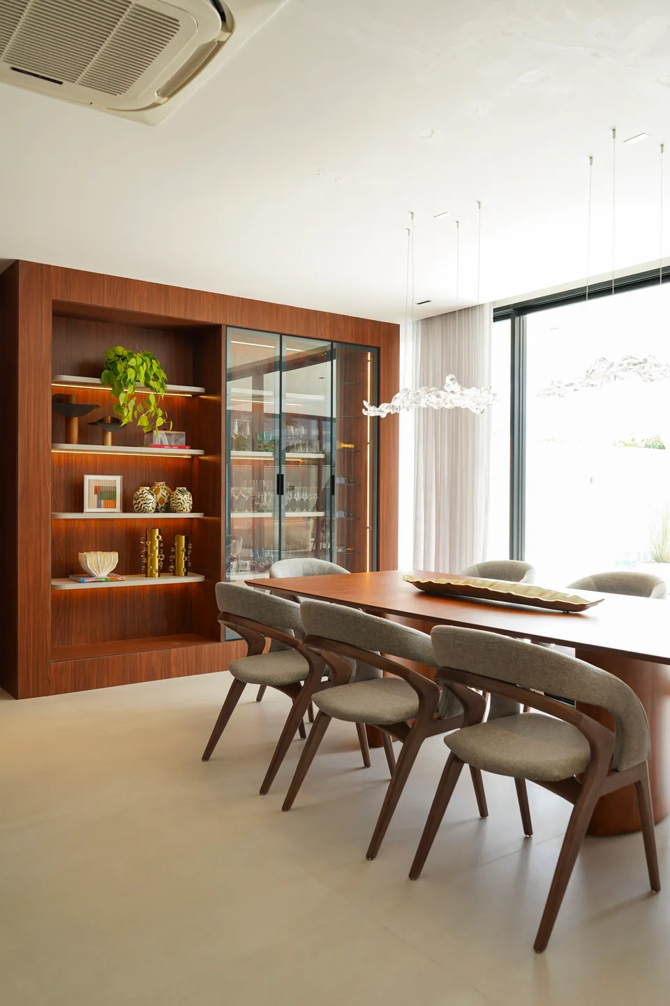 Sala de jantar ampla com mesa longa, oito cadeiras e grandes janelas com cortinas leves