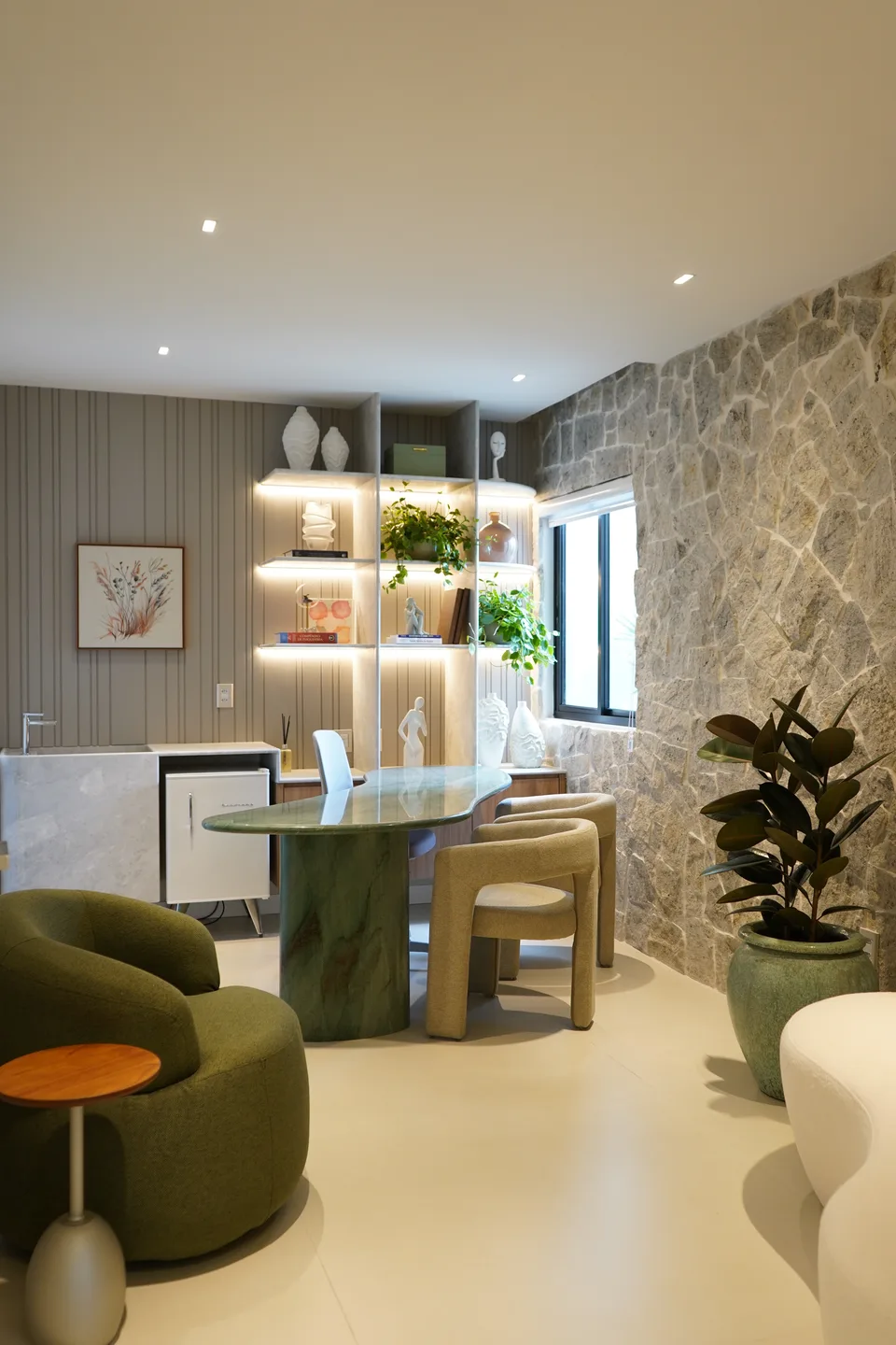 Sala de atendimento com parede de pedra natural, mesa orgânica de pedra verde, poltrona verde e estante iluminada