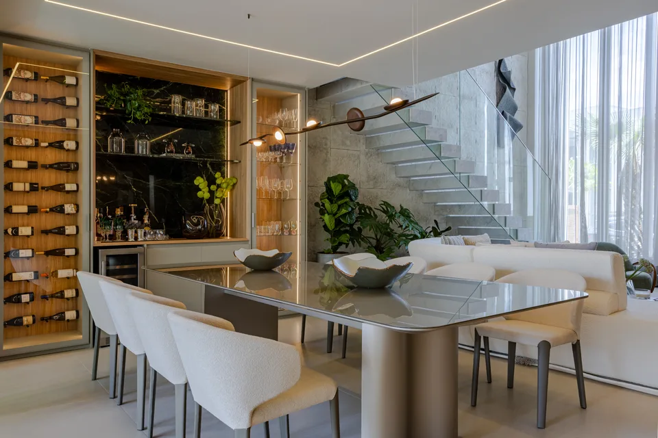 Sala de jantar com sanca acesa, adega iluminada e pendente sobre a mesa de tampo de vidro